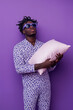 © Pacharee - Sleepy person in pajamas holding a pillow on a purple background.