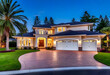 © Morning - A stunning modern mansion with a beautifully landscaped garden a circular driveway warm lighting and an inviting entryway at twilight.