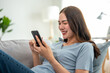 © Kawee - Asian beautiful woman sitting on sofa and swipe mobile phone in house