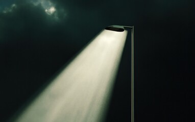 Fototapete - Single lamppost illuminating a dark night scene. A beam of light cuts through the darkness, casting a spotlight effect. Dark clouds fill the background