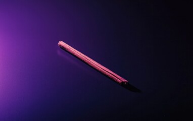 Poster - A single, slender brown object rests on a dark purple surface. The object is slightly textured, and the background is subtly speckled with light. The lighting casts a soft glow