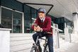 © Jelena - Senior Businessman Using Mobile Phone While Resting on Bicycle by Office Building
