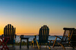 © Mint Images - Adirondack chairs on the beach at sunset, an orange sunset glow on the horizon.