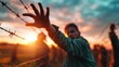© Nena Photo - A troubled individual extends their hand through barbed wire, symbolizing struggle and desperation under a dramatic sunset sky, evoking deep emotions of hope and resilience.