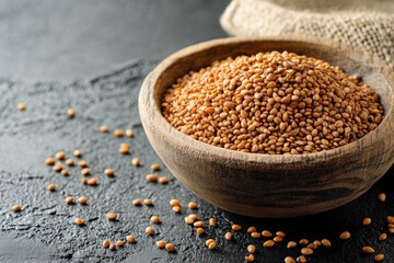 Poster - Close-up view of a wooden bowl filled with golden sesame seeds on a dark stone surface