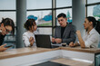 © qunica.com - A team of business professionals engaged in a discussion around a table in a modern office. The group is focused on a laptop while interacting, suggesting teamwork, communication, and collaboration.