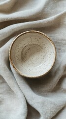 Aufkleber - This delicate ceramic bowl features unique speckled patterns, showcasing artisanal skill. Placed atop soft, textured linen, it creates a serene atmosphere perfect for any occasion