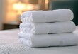 © Moritz - Stack of clean, white towels neatly folded on a bed in a hotel room, ready for guests, conveying comfort and hospitality