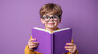 © Olga Ко - Niño sonriente leyendo un libro sobre un fondo morado.