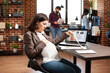 © DC Studio - Pregnant businesswoman sitting and reviewing research data at office desk with laptop nearby. Focused expectant mother going through company paperwork and gently caressing her pregnancy belly.