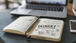 © watz - Open notebook with Delivery written on the page next to a pen phone and blurred laptop.