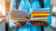© Bagas - Student holding two stacks of papers.