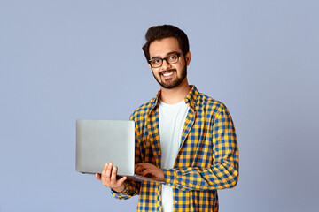 Poster - Happy Indian guy with laptop computer working or studying online on lilac background
