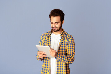 Poster - Smiling Indian man studying or working online on tablet computer against lilac background
