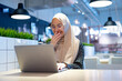 © maya1313 - Cheerful muslim lady in hijab working online at cafe, using laptop, copy space. Side view of smiling arab woman freelancer typing on laptop, enjoying her distant job, Muslim working woman concept.