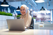 © maya1313 - Cheerful muslim lady in hijab working online at cafe, using laptop, copy space. Side view of smiling arab woman freelancer typing on laptop, enjoying her distant job, Muslim working woman concept.