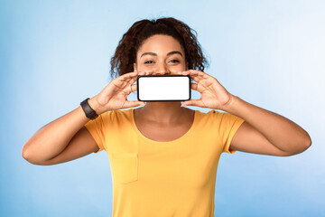 Poster - Hot offer, online sale. Pretty African American woman covering her mouth with blank cellphone over blue studio background, mockup. Cool lady advertising new awesome mobile app or website
