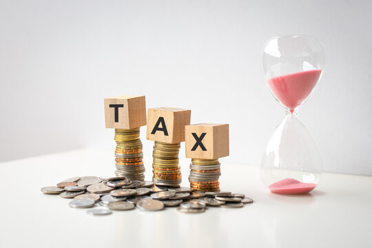 Tax word on wood blocks on top of coins and next to hourglass.