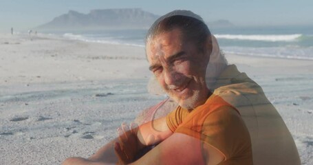 Poster - Sitting on sandy beach, man smiling with ocean and mountain in background