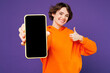 © ViDi Studio - Young happy woman she wear orange hoody casual clothes hold in hand use mobile cell phone with blank screen workspace area show thumb up isolated on plain purple background studio. Lifestyle concept.
