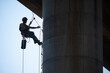 © oscar - Rope access technician securing himself with a rope on concrete bridge pillar