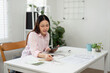 © wichayada - Work-Life Integration and Comfort. A woman manages her home office activities with confidence and style.