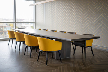 Aufkleber - Long wooden table with yellow and dark gray chairs in a modern office, showcasing a sleek and professional workspace near a window
