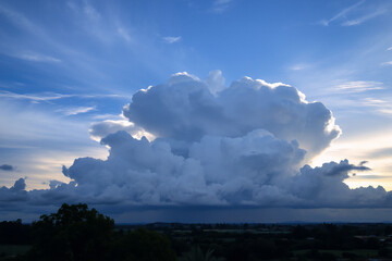 Aufkleber - A massive, bright cloud formation fills the sky, contrasting with the dark land below and a soft sunset glow on the horizon.