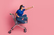 © deagreez - Young Woman Sitting in Shopping Cart Posing Enthusiastically On a Vibrant Pink Background
