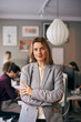 © Maskot - Portrait of confident female business professional standing with arms crossed in office