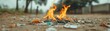 © Kakabe - A close-up view of burning trash on a dirt path, with a blurred figure in the background, The image highlights issues of pollution and waste management