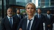 © lililia - Businesswoman stands confidently in front of her team of men, all dressed in suits, smiling and exuding team spirit in a bright office.