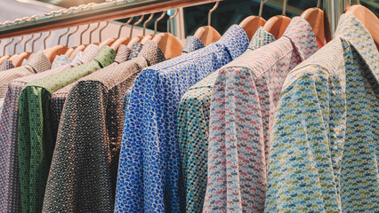 Poster - A rack of clothes with a variety of colors and patterns, including green, blue, and red. The clothes are hanging on a rack, and the colors and patterns are diverse