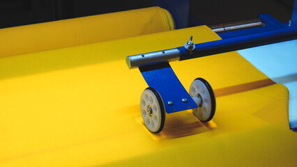 Aufkleber - A blue and white machine is on a yellow fabric. The machine is used to cut fabric