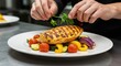 © Photowizard - Chef garnishing grilled chicken breast on a plate with vegetables and parsley in a professional kitchen