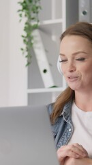 Poster - A cheerful young woman participates in a virtual meeting with trendy headphones while seated at a modern desk in a bright office designed to boost productivity and stimulate creativity