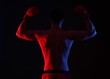 © New Africa - Man in boxing gloves showing his biceps on black background in neon lights, back view