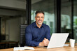 © insta_photos - Portrait of happy business man leader of middle age working on laptop in office. Senior executive manager or investor using computer sitting at desk. Smiling older professional businessman at work.