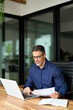 © insta_photos - Busy mature male bank manager executive working on laptop checking paper financial report in office. Middle aged professional business man using laptop computer reading document at work, vertical.