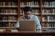 © nian - Focused Indian student guy sit at desk in library, studying, e-learning, improve math or language subject knowledge, preparing to higher education institution admission using laptop. Gen Z, education