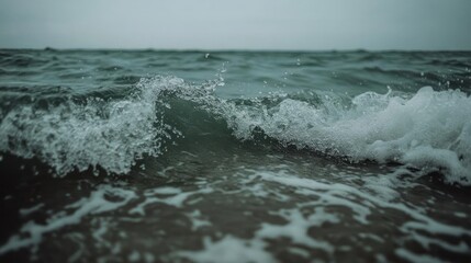 Poster - Close-up view of ocean waves crashing on shore with turquoise water and white foam dark moody overcast sky atmospheric coastal landscape