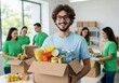 © Poetra RH - charity, donation and volunteering concept - happy smiling male volunteer with food in box and international group of people at distribution or refugee assistance center