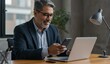 © sitifatimah - Hispanic man using smartphone and laptop in modern office setting, engaged in work and communication, showcasing productivity.
