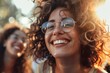 © HISTOCK - Young woman with curly hair and glasses happily enjoying a music festival with her friends