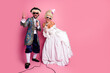 © deagreez - Elegant couple dressed in vibrant historical costumes enjoying a playful singing performance on a pink background