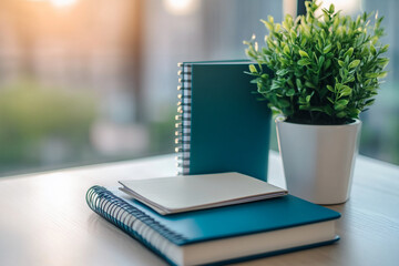Poster - Teal notebooks and a small plant in a white pot on a light wood table near a window, showcasing a calm workspace or office scene, ideal for a minimalist aesthetic or productivity concept