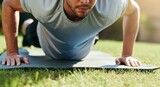 Man in athletic wear performing push-ups on mat outdoors