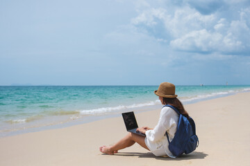 Wall Mural - a female traveler using and working on laptop computer while sitting on the beach