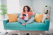 © deagreez - Excited young woman playing video games on a colorful sofa, enjoying a relaxing day in a casual and stylish home setting