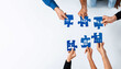 © InfiniteFlow - Hands of diverse individuals come together to assemble blue puzzle pieces symbolizing collaboration and innovative problem-solving in a modern business context. Amity